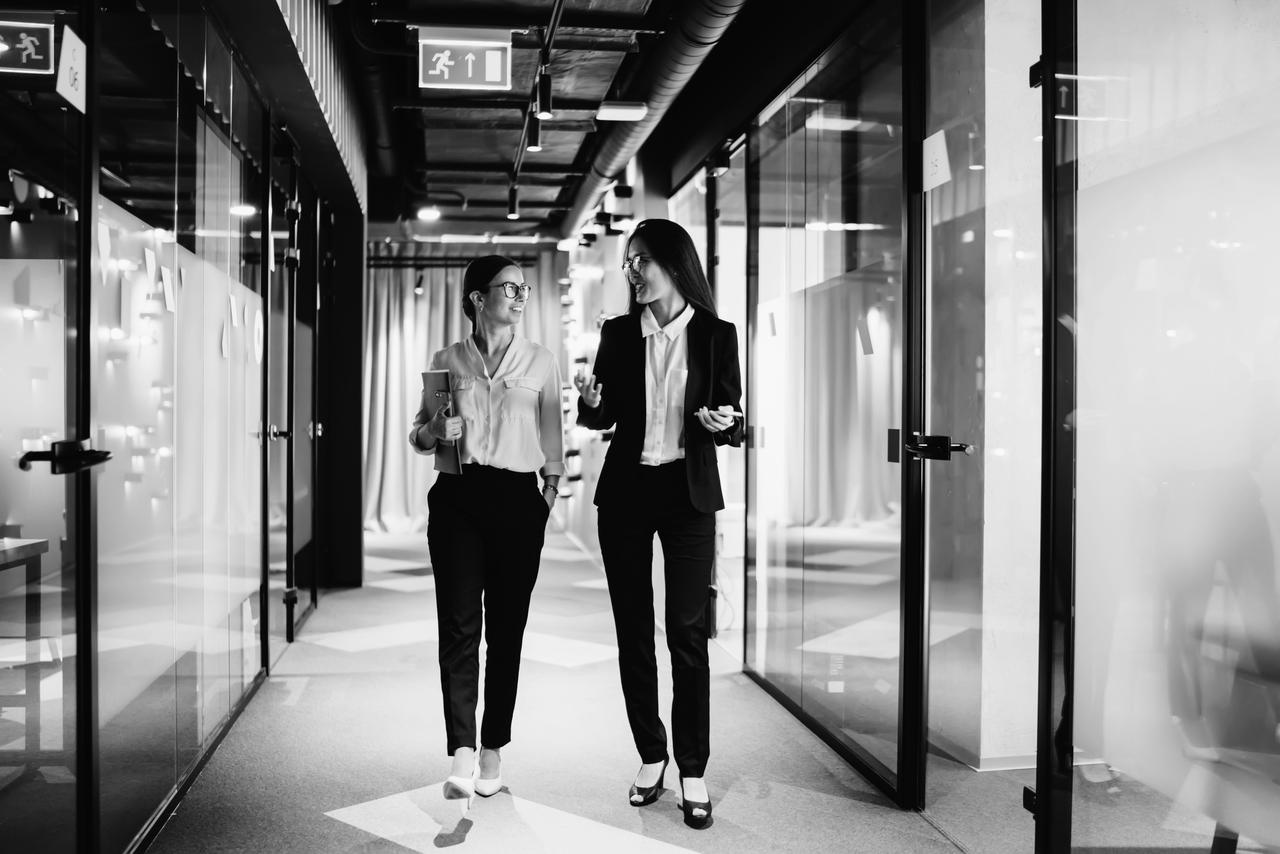 Confident women walking and talking in an office Successful female executive managers walking in corporate hallway
