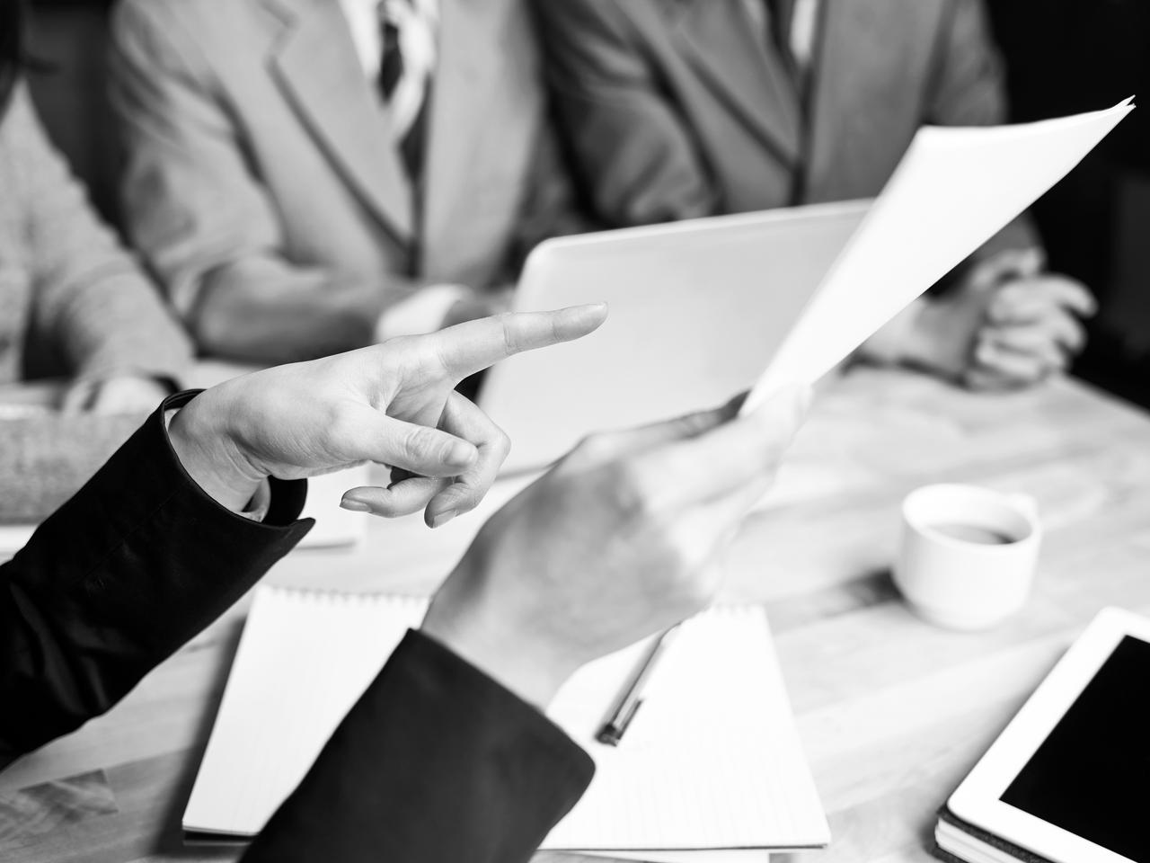 A hand is pointing at a paper document during a meeting Business people reviewing sales performance in a meeting.