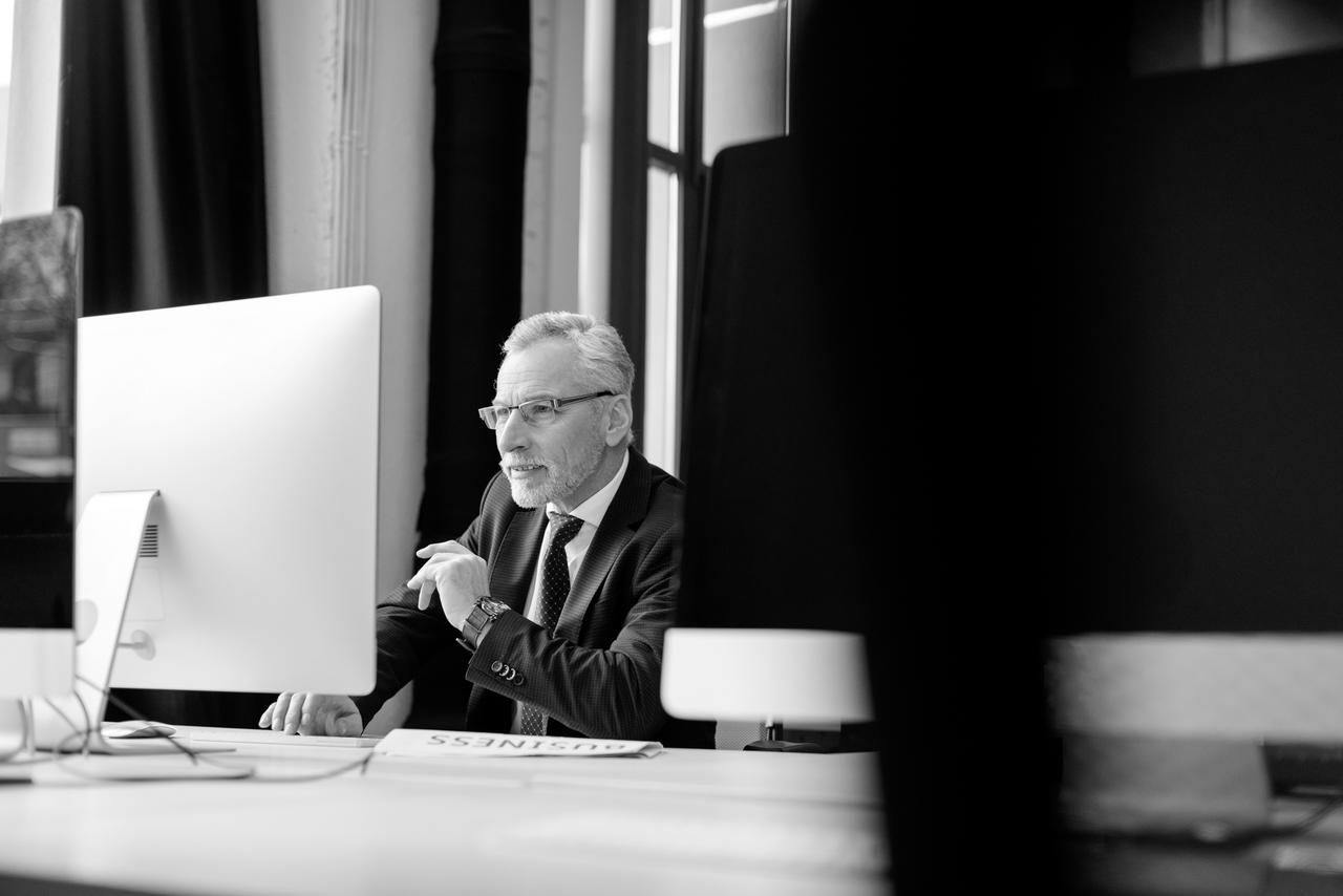 Senior businessman in front of computer screen and smiling Selective focus of senior businessman working on computer in office