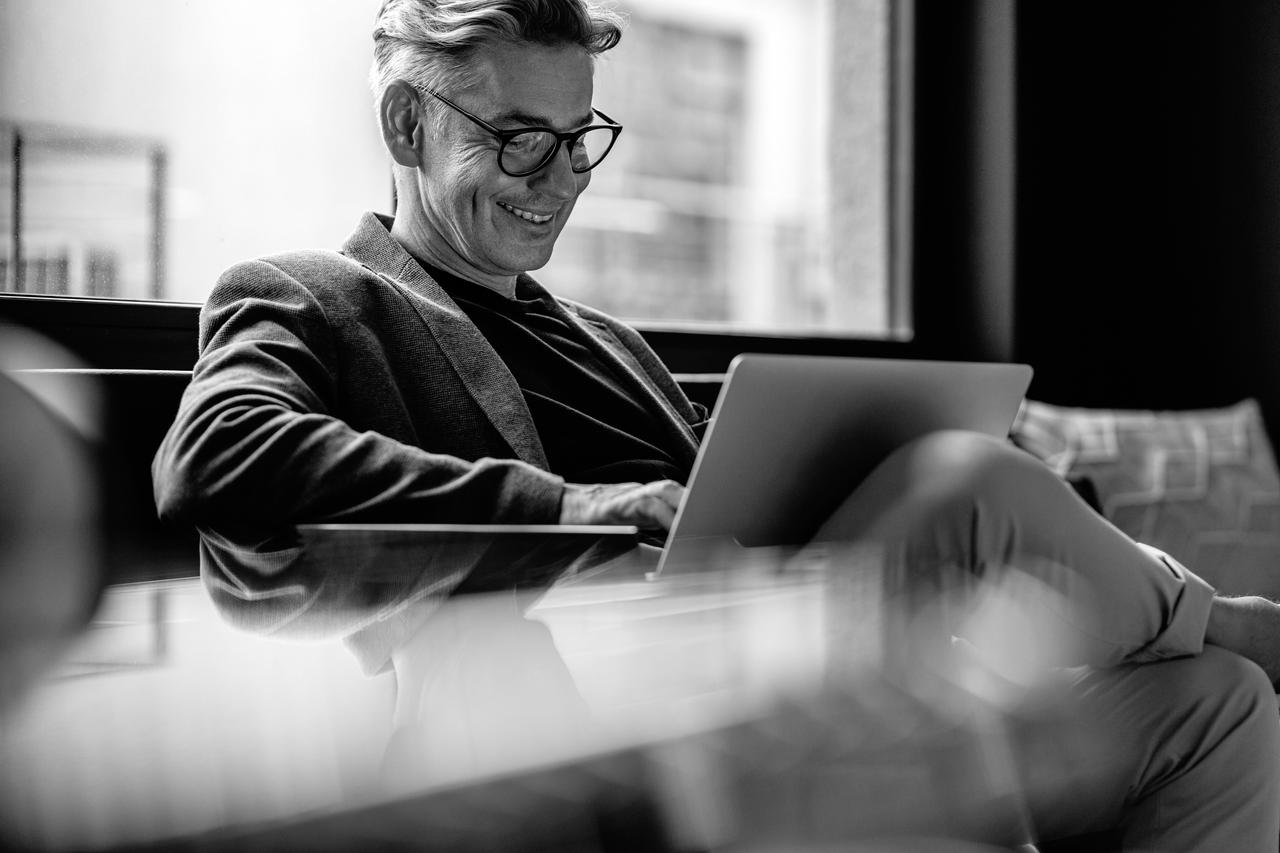 Male business professional with laptop working Smiling businessman sitting in office lobby working on a laptop